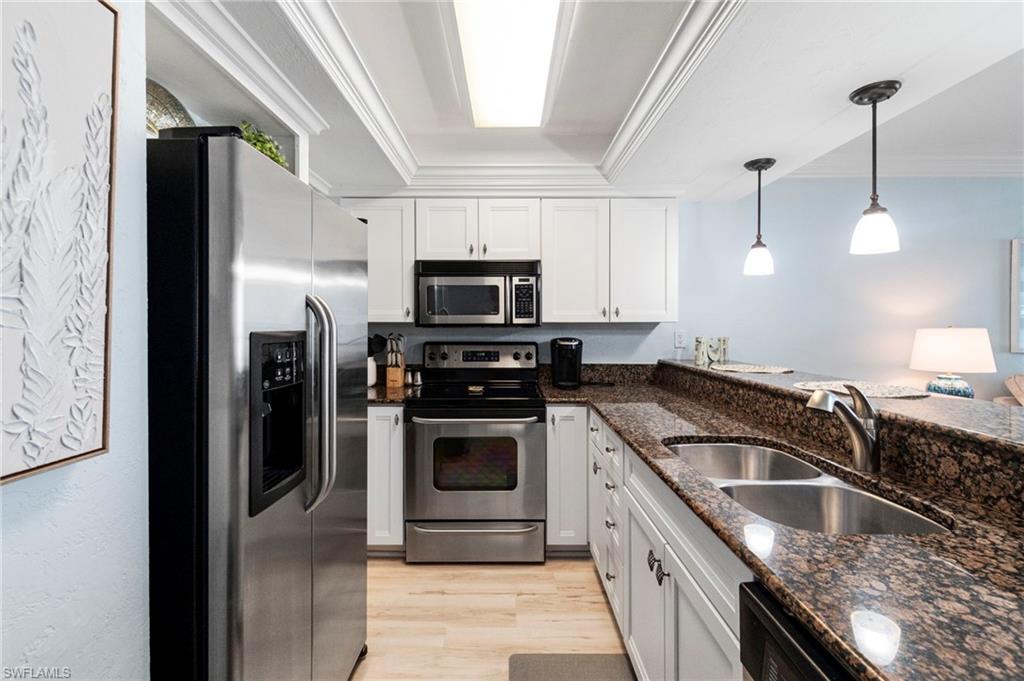 Kitchen featuring white cabinetry, stainless steel appliances, a double basin sink, polished stone countertops, and wood-finish flooring