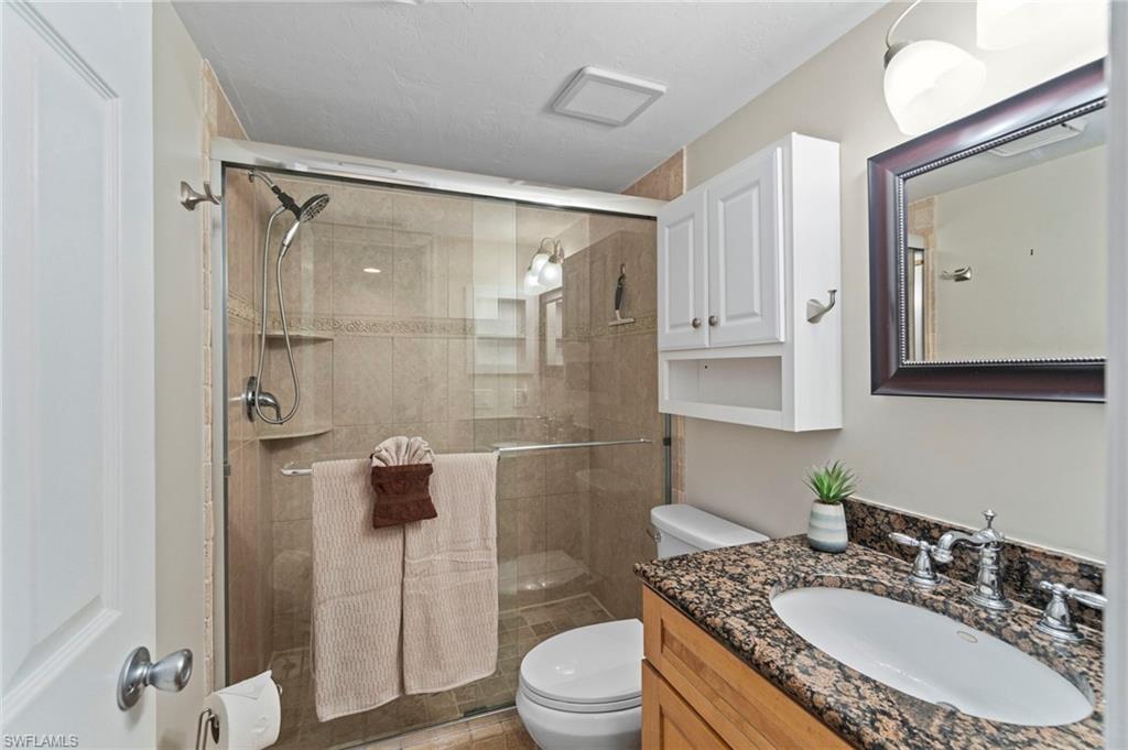 Full bathroom featuring a glass-enclosed shower with tile surround and integrated shelving, a white vanity cabinet with a stone countertop, an undermount sink, and a framed mirror