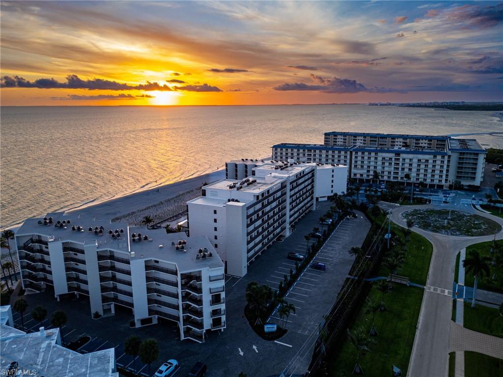 Beachfront condominium buildings featuring multiple balconies, paved parking areas, and manicured landscaping