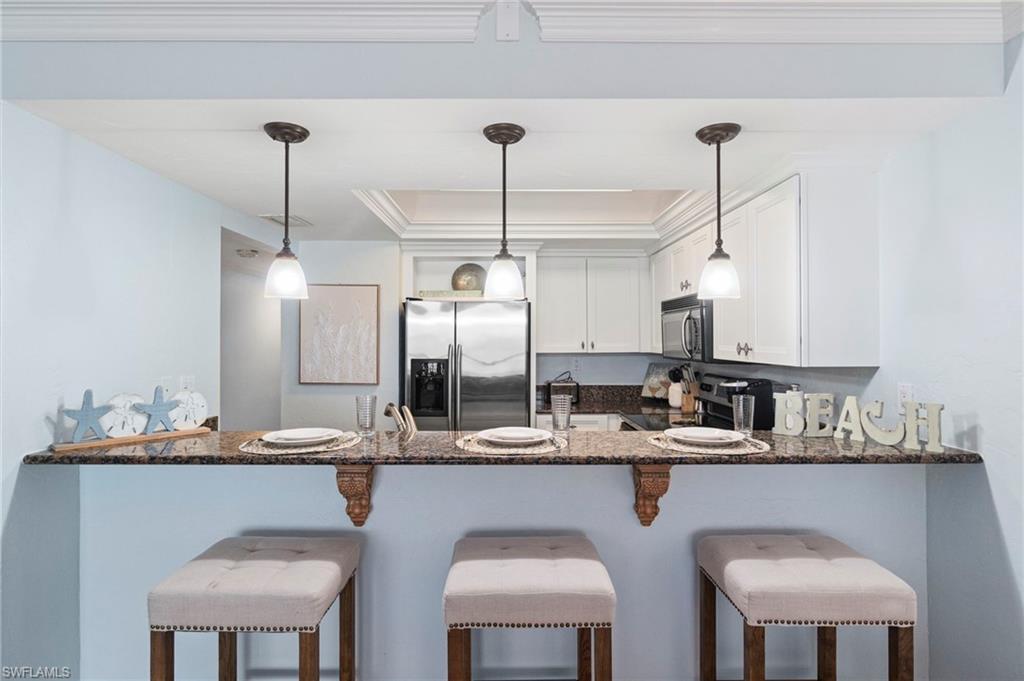 Kitchen breakfast bar with a granite countertop, three pendant lights, and white upper cabinetry