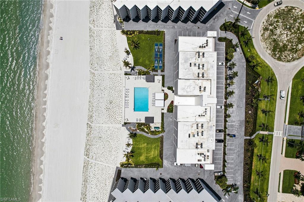 Coastal property featuring beachfront access, a rectangular swimming pool, landscaped green spaces, a tennis court, and ample parking