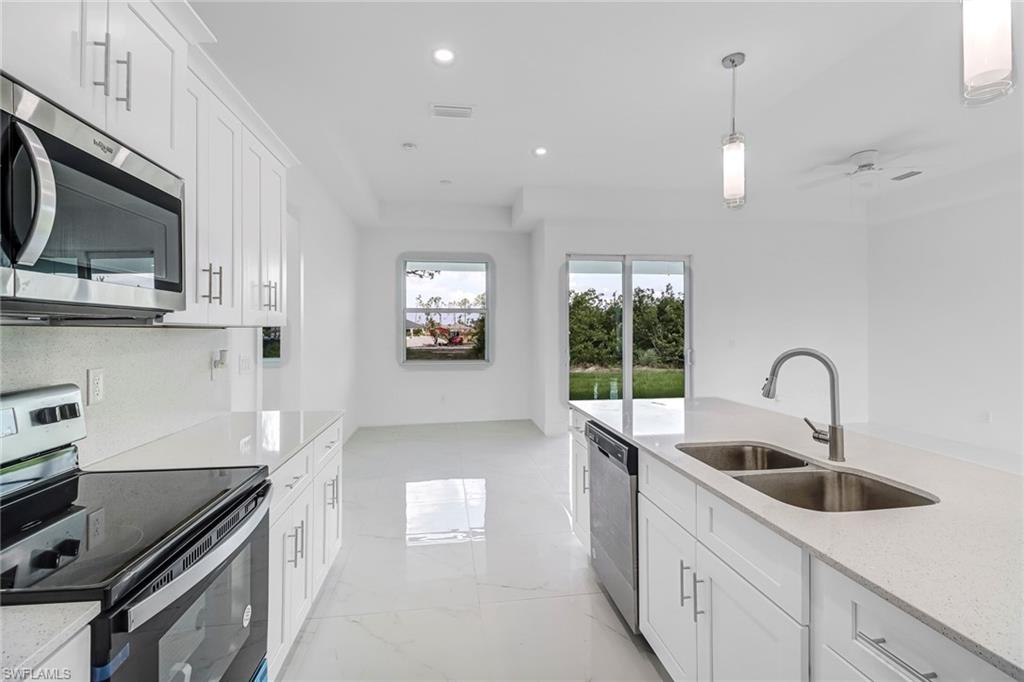 Contemporary kitchen featuring white cabinetry, stainless steel appliances, a center island with a double basin sink, and pendant lighting