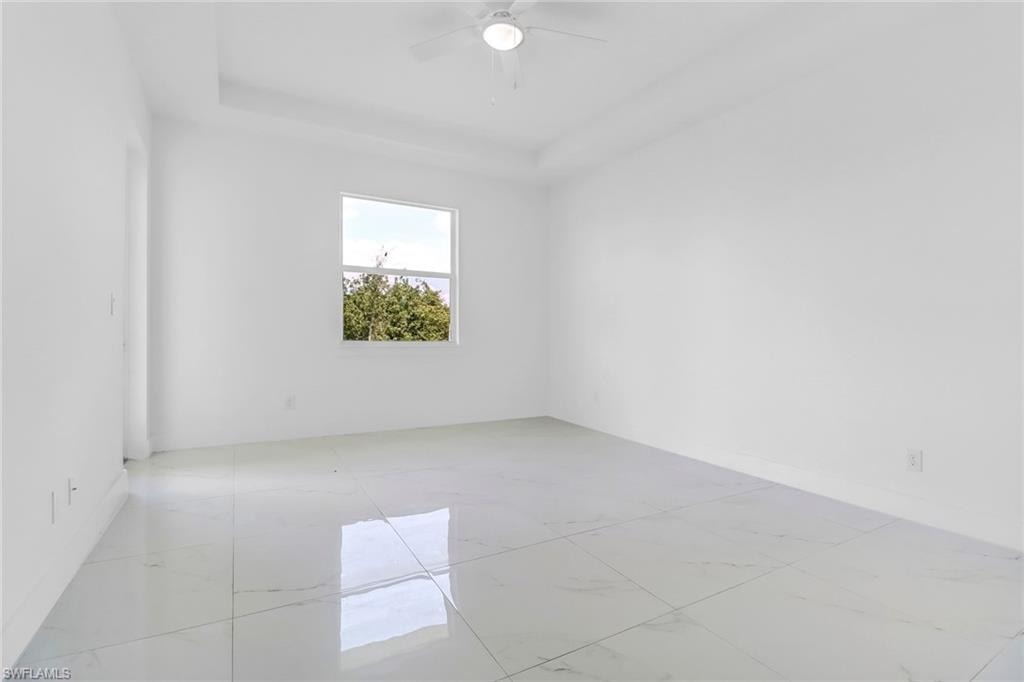 Spacious room featuring large format tile flooring, a window offering exterior scenery, a ceiling fan, and a tray ceiling detail
