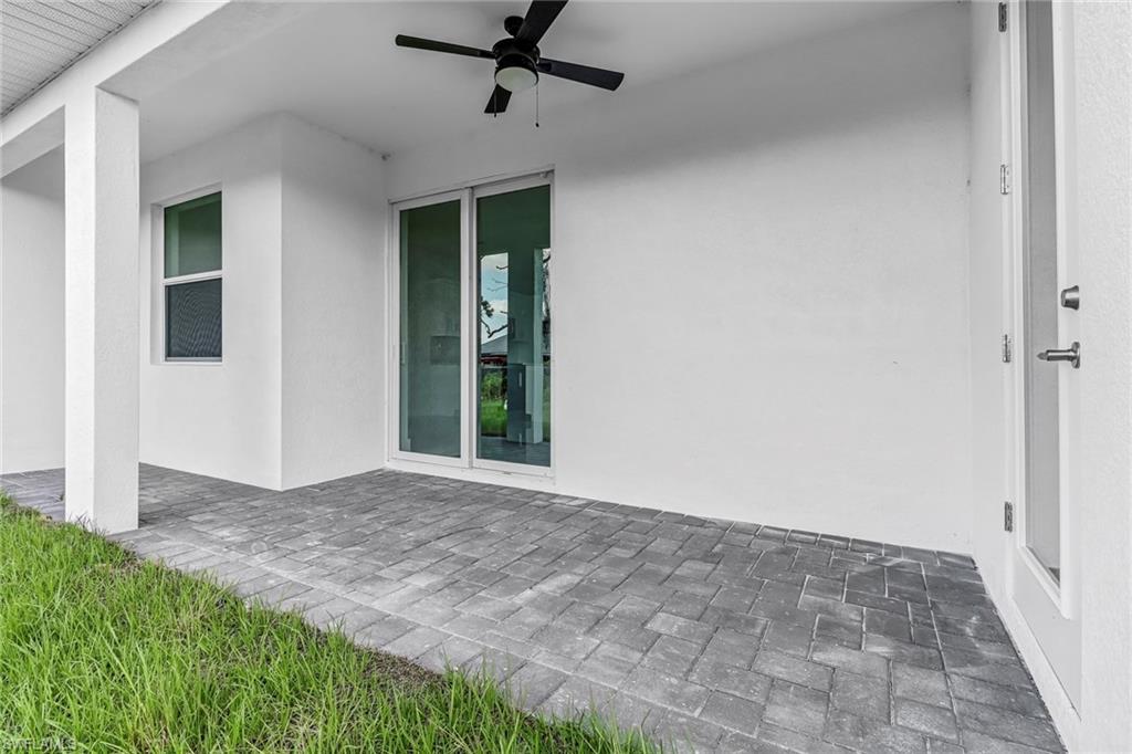 Covered patio featuring a ceiling fan, white stucco exterior, and grey paver flooring