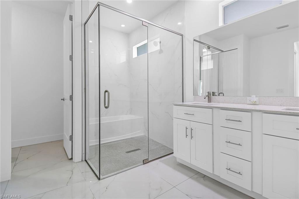 Modern bathroom featuring a glass-enclosed shower with a built-in tub, large format tile flooring, and a double vanity with stone countertops and undermount sinks