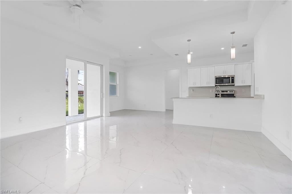 Spacious interior featuring white tile flooring throughout, a modern kitchen with white cabinetry and stainless steel appliances, and a ceiling fan
