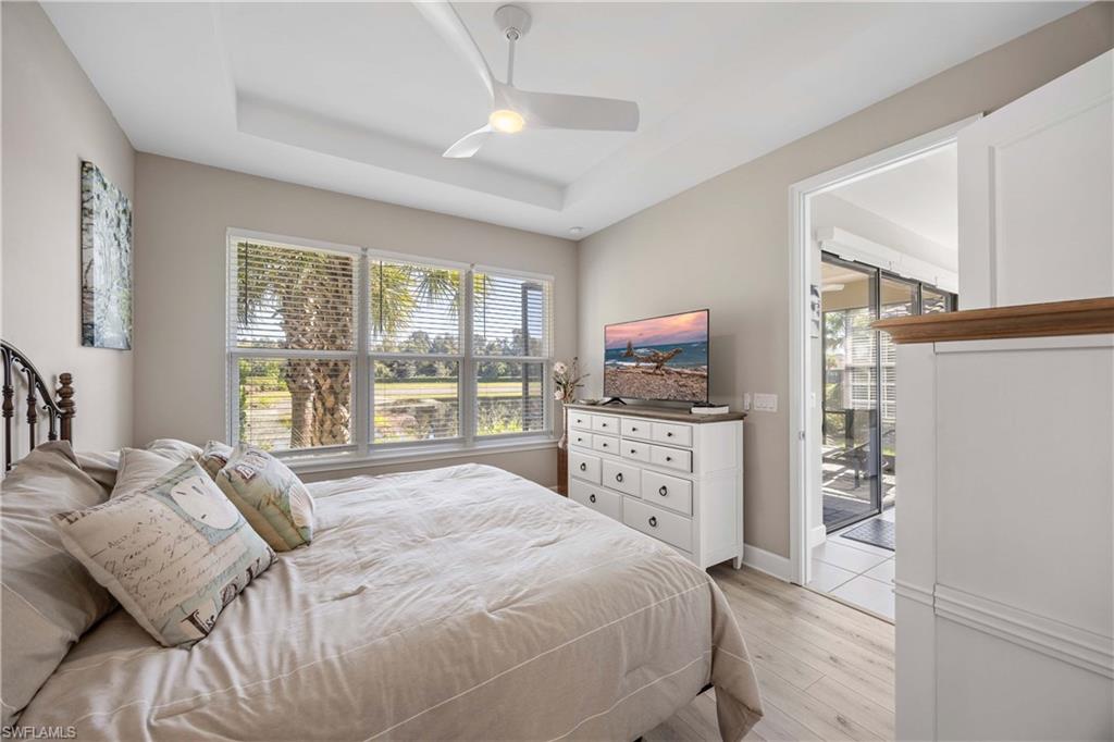 Bedroom with multiple windows, light wood-style floors, a tray ceiling, and a ceiling fan