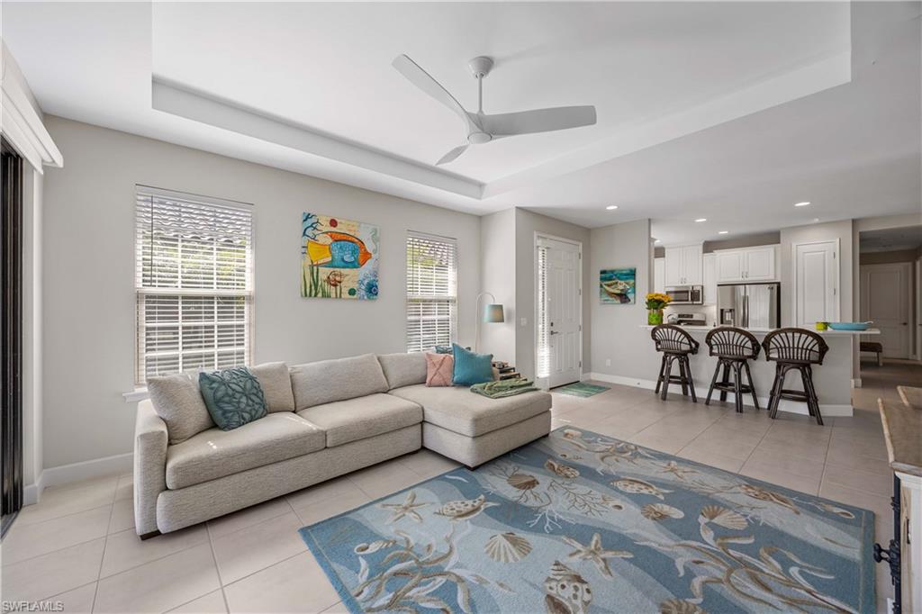 Living room with light tile patterned floors, a raised ceiling, ceiling fan, and recessed lighting