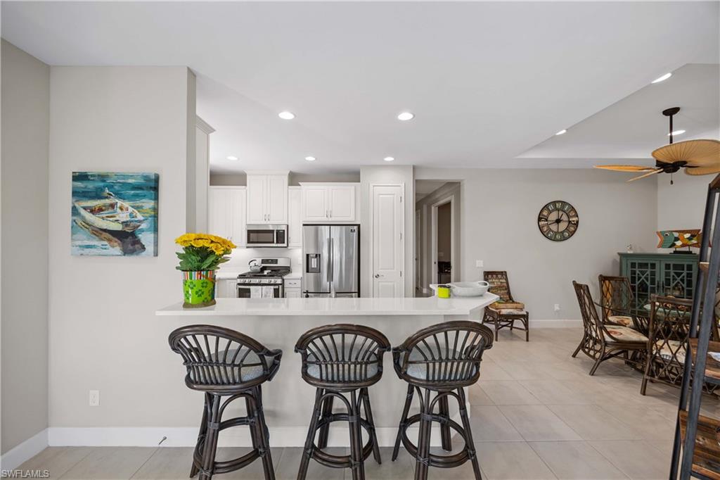 Kitchen featuring a breakfast bar, light tile patterned flooring, stainless steel appliances, a peninsula, and white cabinetry
