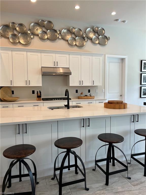 Kitchen featuring white cabinetry, stainless steel range hood, integrated gas cooktop, center island with seating, and light-toned countertops