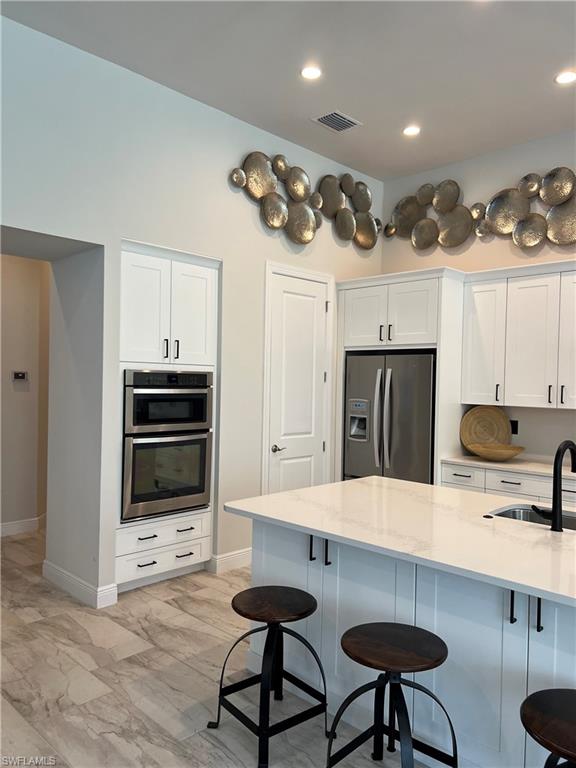 Kitchen featuring white shaker cabinetry stainless steel double wall ovens, a large center island with a white countertop, and wood-finish flooring