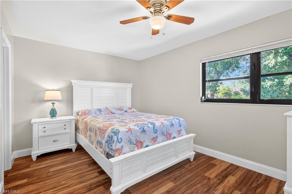 Wood-finish flooring throughout, featuring a window with exterior tree scenery, a ceiling fan with light fixture, and light-toned walls
