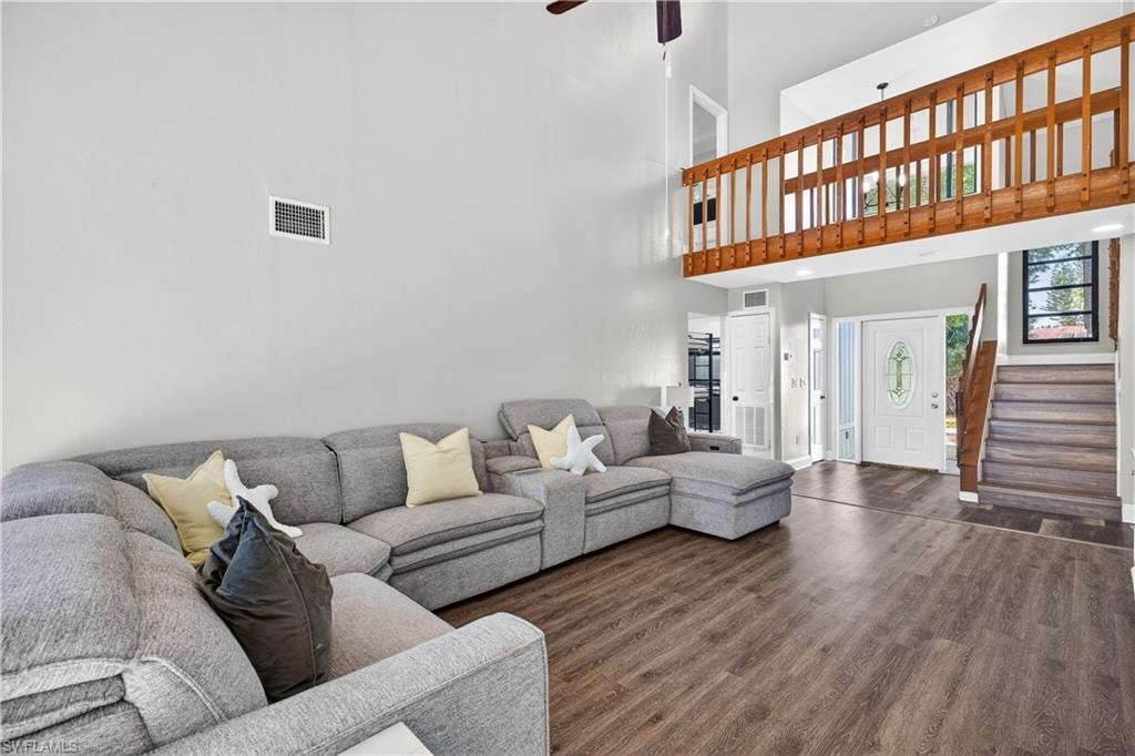 Spacious living area featuring high vaulted ceilings, wood-finish flooring, a wood-railed loft, and a prominent staircase