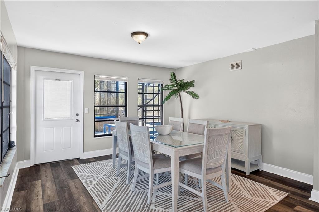 Dining area featuring wood-finish flooring, light gray wall paint, a white paneled door with an integrated blind, and multiple windows with black framing