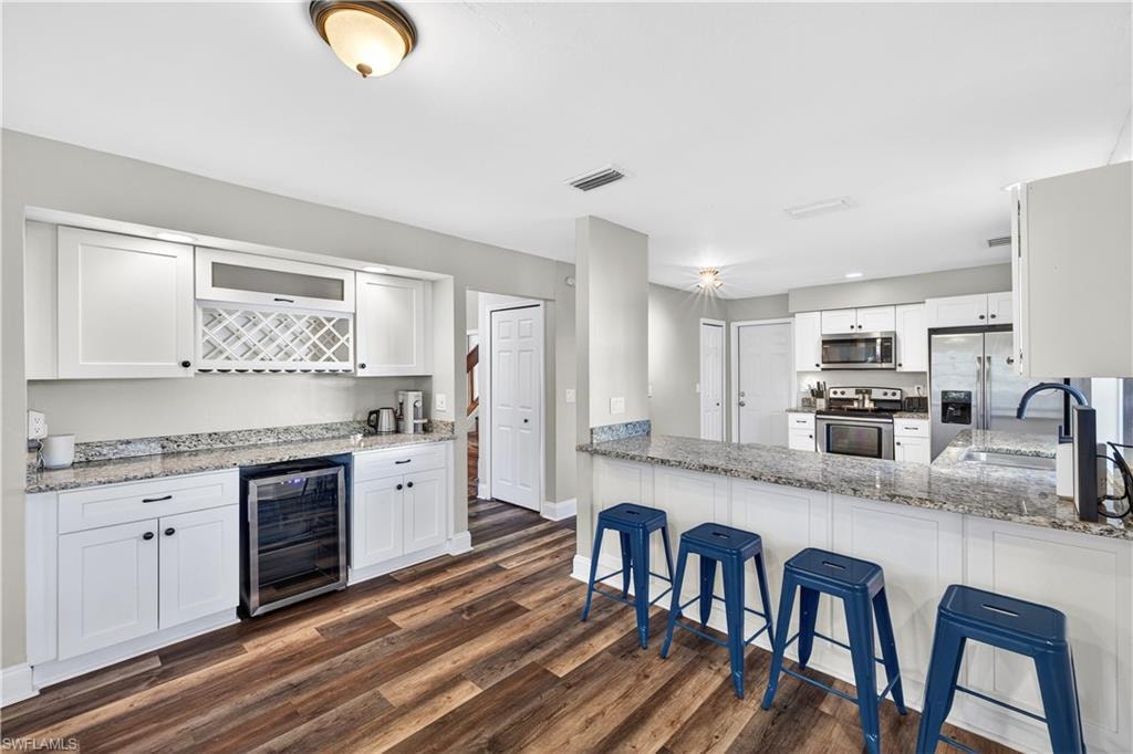 Open-concept kitchen featuring white shaker cabinetry, granite countertops, stainless steel appliances, a breakfast bar, and wood-finish flooring