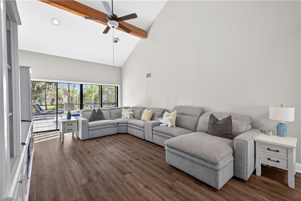 Spacious living area featuring wood-finish flooring, a soaring vaulted ceiling with an exposed wood beam, and a ceiling fan