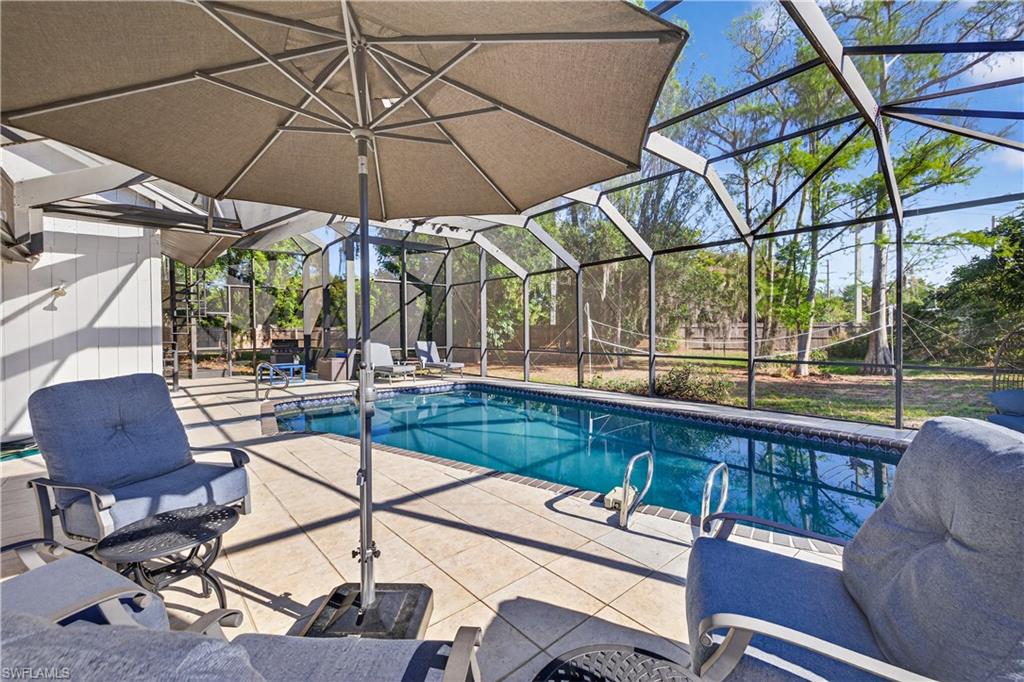 Screened swimming pool enclosure featuring a rectangular pool, light-toned patio pavers, and a white exterior wall