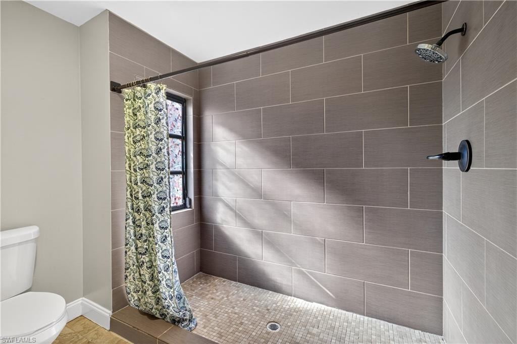 Shower stall featuring rectangular gray wall tiles, mosaic tile flooring, a window, and a matte black shower head and fixture