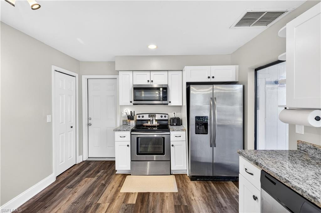 Kitchen featuring white cabinetry, granite countertops, stainless steel appliances, wood-finish flooring, and recessed lighting