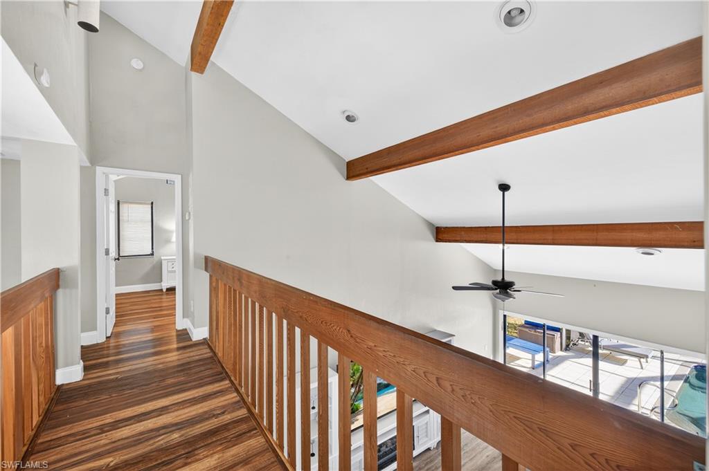 Upper-level hallway featuring wood-finish flooring, wood railings, vaulted ceilings with exposed wood beams, and recessed lighting