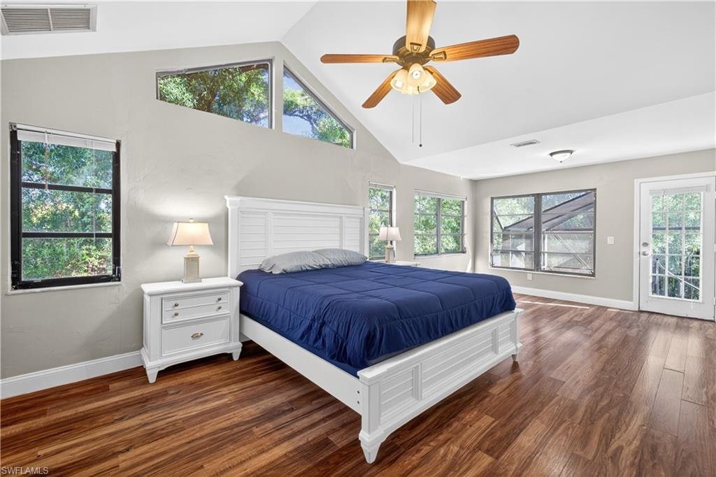 Vaulted ceiling room featuring wood-finish flooring, a ceiling fan with integrated lighting, multiple windows, and a glass-paneled door
