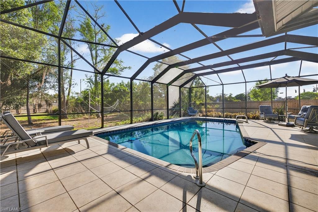 Screened-in pool enclosure featuring a rectangular swimming pool, light-toned paved decking, and a perimeter safety railing
