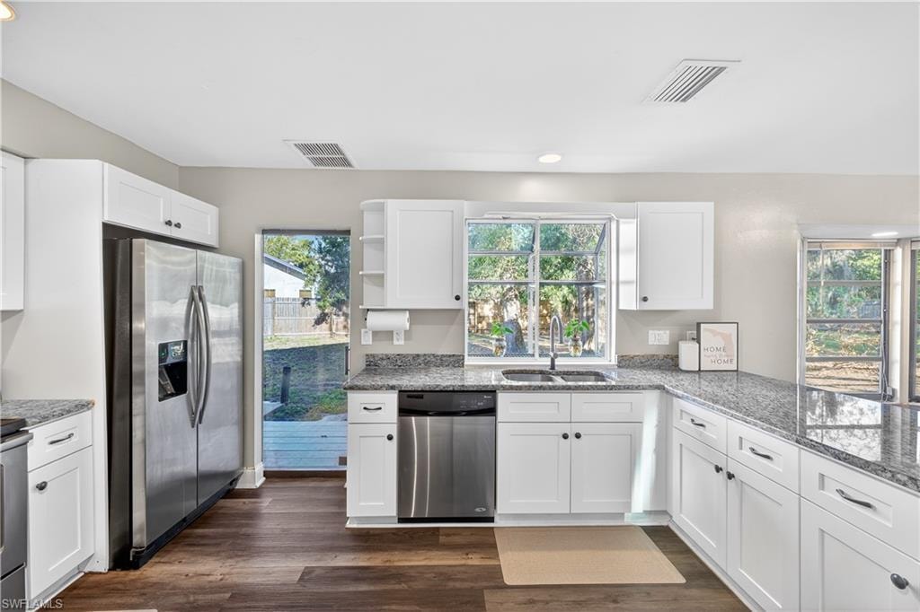 Modern kitchen featuring white shaker cabinetry, stainless steel appliances, speckled countertops, and wood-finish flooring