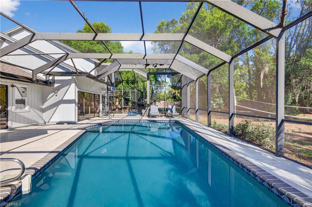 Screened enclosure featuring an in-ground swimming pool with a tiled edge, concrete decking, and direct access to the white exterior of the home through large sliding glass doors