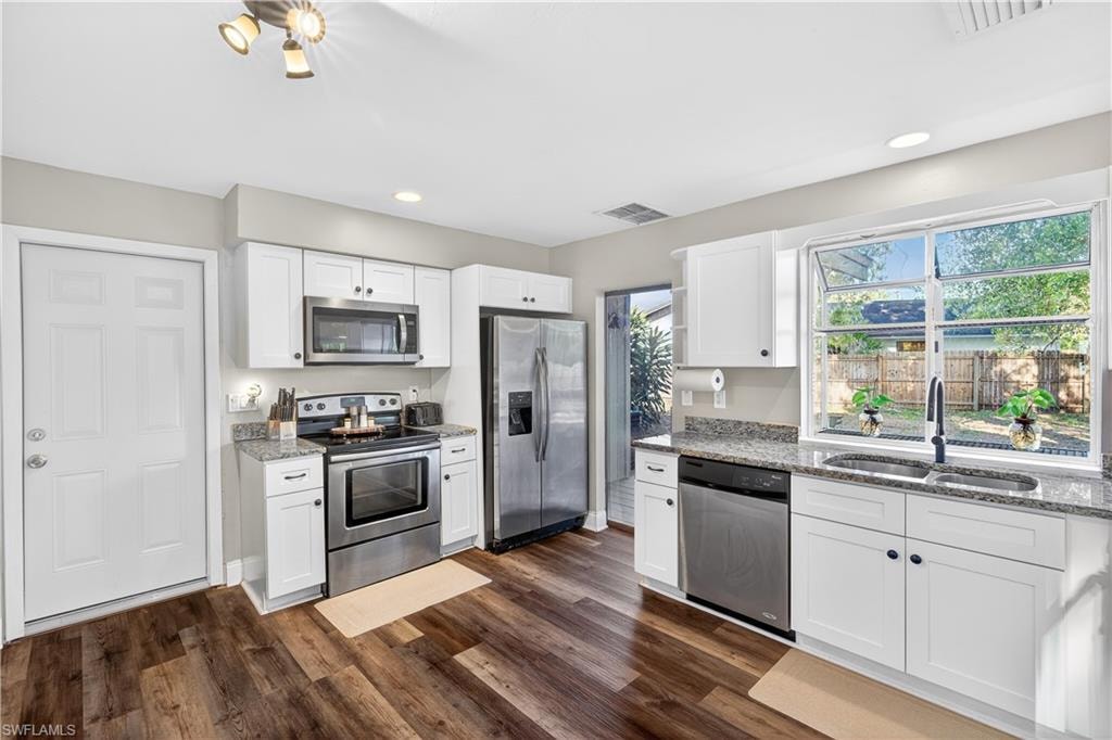 Modern kitchen featuring white cabinetry, granite countertops, stainless steel appliances, wood-finish flooring, and a large window above the sink