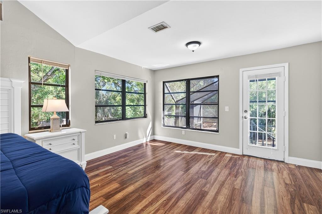 Spacious room featuring wood-finish flooring, a vaulted ceiling, multiple windows, and a glass-paneled door