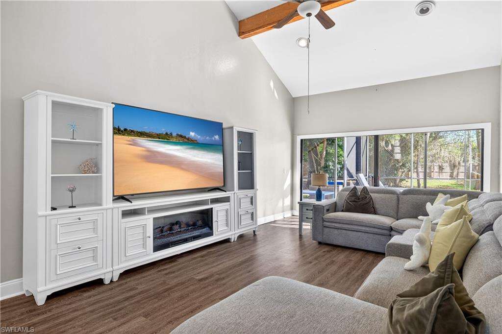 Vaulted ceilings with exposed wood beam, wood-finish flooring, and large sliding glass doors opening to the outdoor area