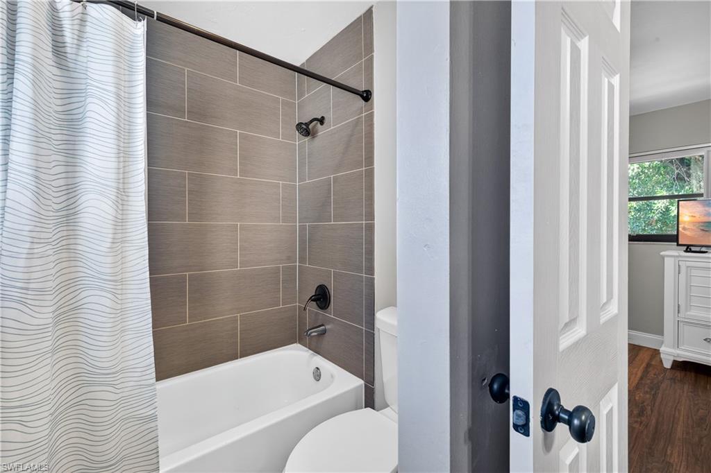 Bathroom featuring a white tub, toilet, and shower with horizontal rectangular tile surround