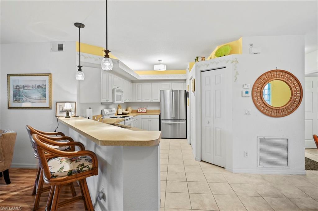 Kitchen with white cabinetry, kitchen peninsula, a kitchen bar, white appliances, and decorative light fixtures