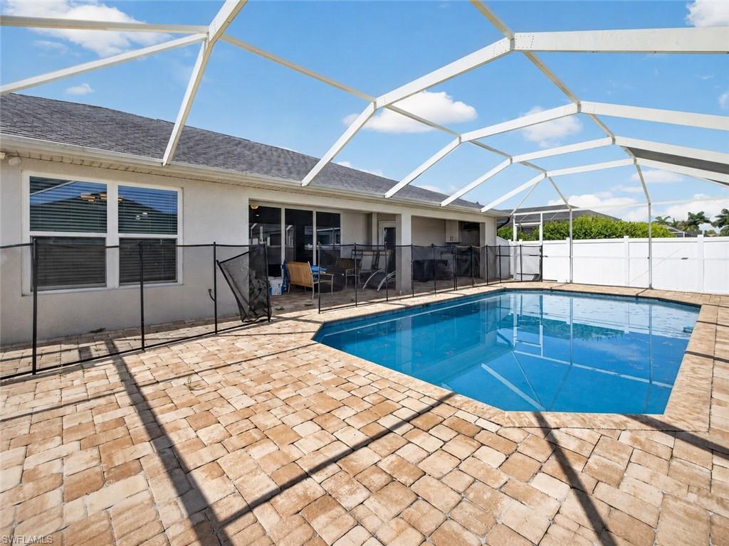 Screened lanai featuring a swimming pool, textured paver decking, and a perimeter safety fence