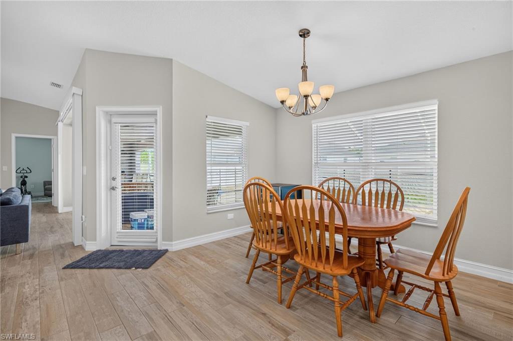 Dining area featuring wood-finish flooring, two windows with blinds, a glass-paned door, and a multi-bulb chandelier