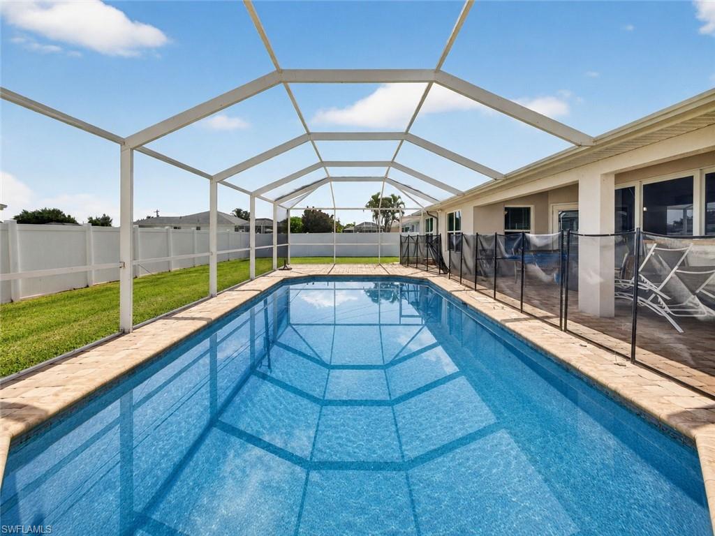 Screened swimming pool enclosure featuring a rectangular pool with a safety fence, paver decking, and a stucco exterior