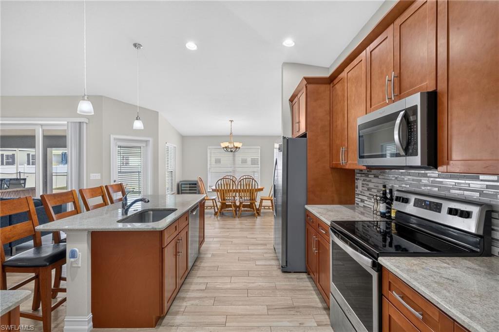 Modern kitchen featuring a breakfast bar with a stainless steel sink, wood-finish cabinetry, light-toned countertops, and stainless steel appliances including a microwave and range