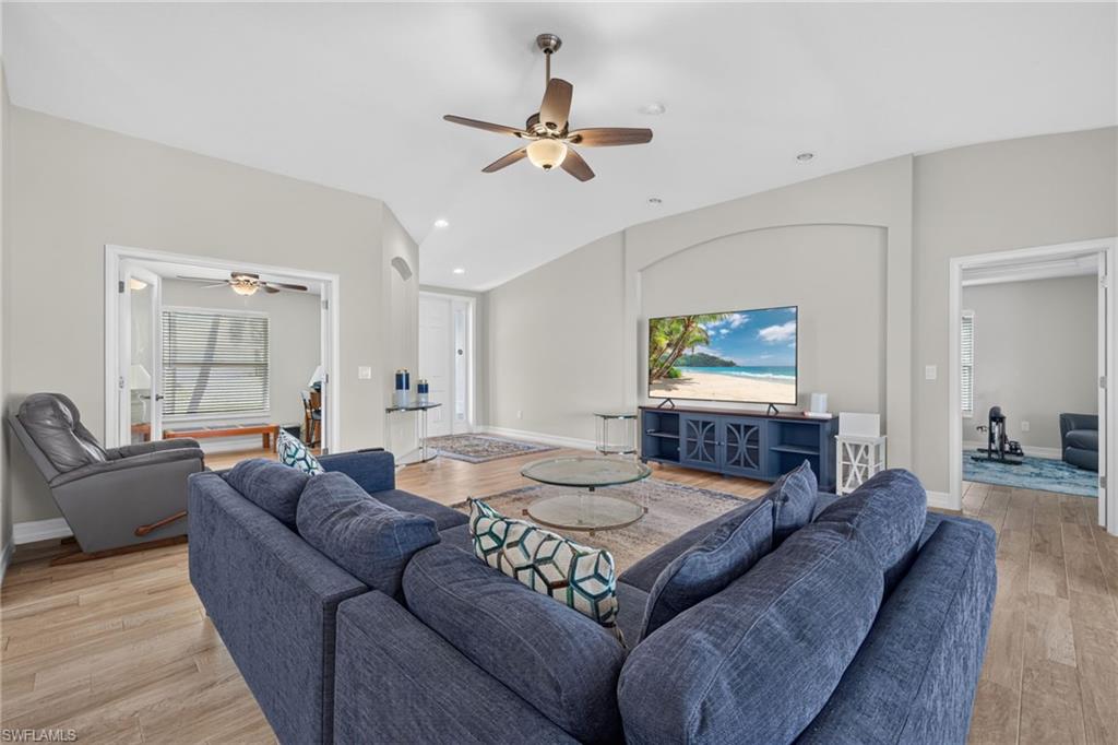 Spacious living area featuring light wood-finish flooring, vaulted ceilings, recessed lighting, and a ceiling fan