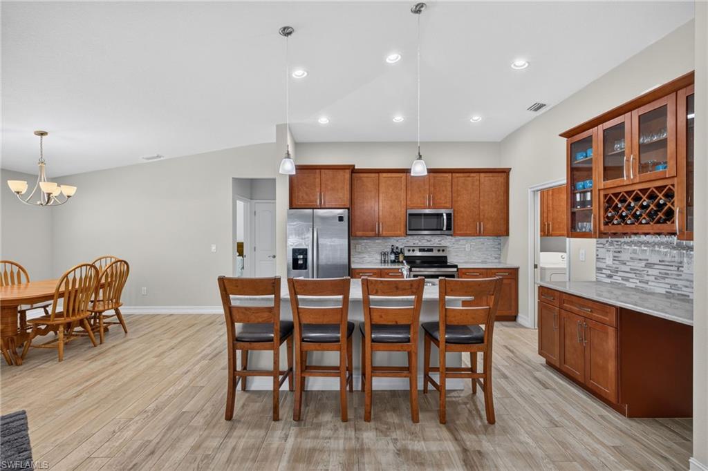 Kitchen featuring wood cabinetry, stainless steel appliances, a tiled backsplash, and an island with pendant lighting