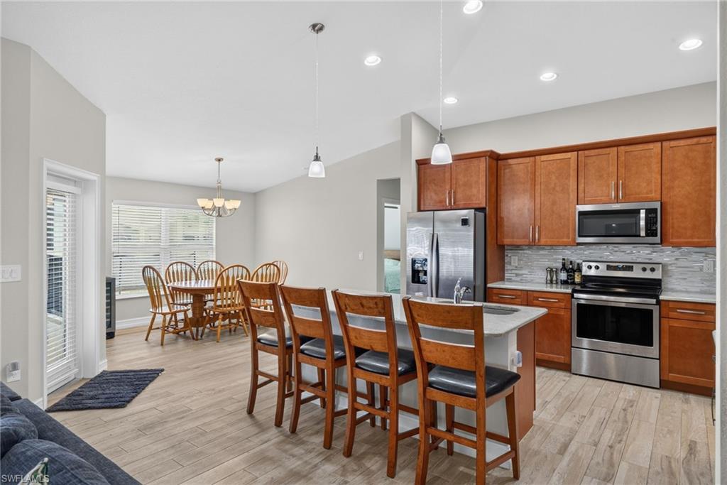Kitchen and dining area featuring warm wood-finish cabinetry, stainless steel appliances, a tiled backsplash, and an island with pendant lighting