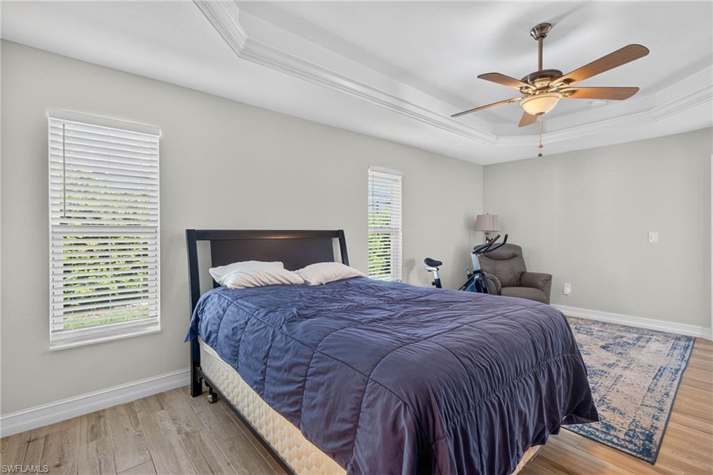 Bright room featuring wood-finish flooring, a tray ceiling with crown molding, and a ceiling fan