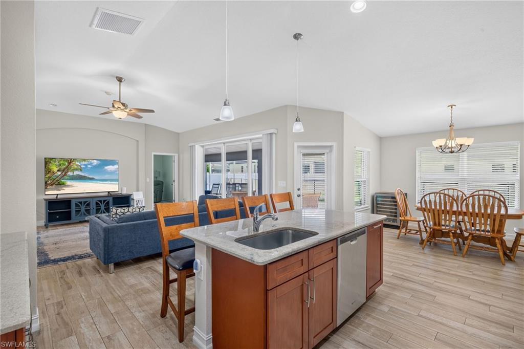 Open-concept living space featuring a central kitchen island with granite-style countertop and integrated sink, wood-finish flooring, and recessed ceiling lighting
