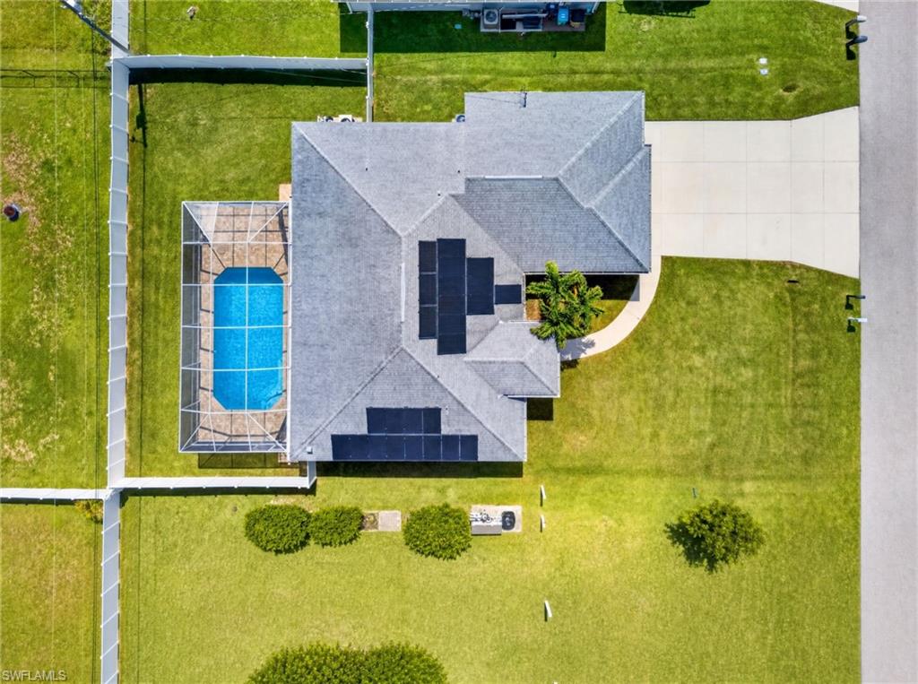Expansive property featuring a screened-in swimming pool, mature landscaping, substantial driveway, and solar panels