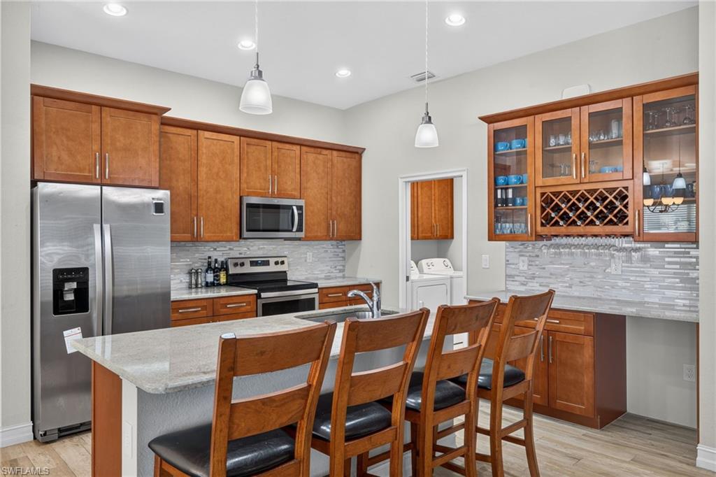 Kitchen featuring a central island with countertop seating, stainless steel appliances, wood-finish cabinetry, and a tile backsplash