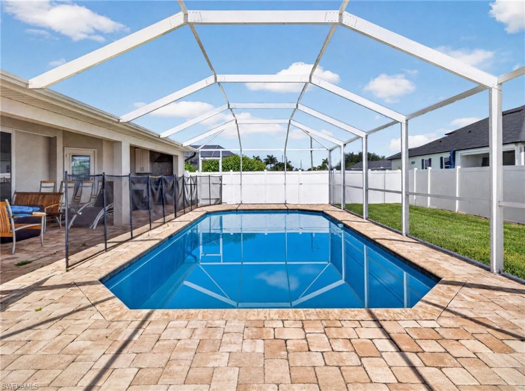 Screened outdoor swimming pool with paver decking, a safety fence, and a white privacy fence