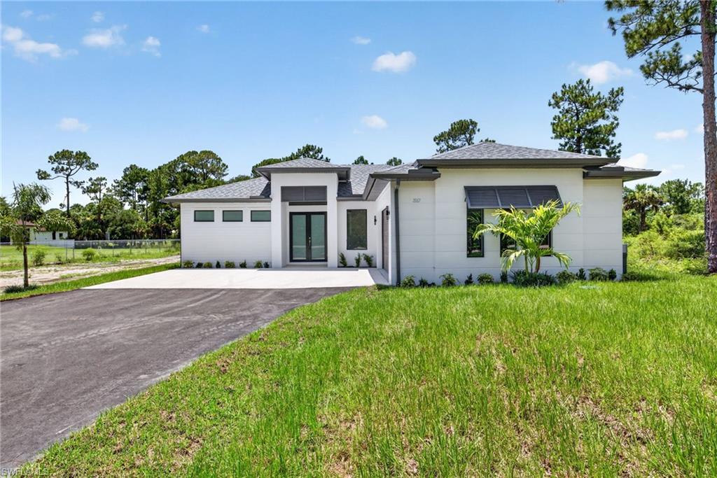 Contemporary architecture featuring a white exterior, a dark shingle roof, a paved driveway, and a concrete entrance pad