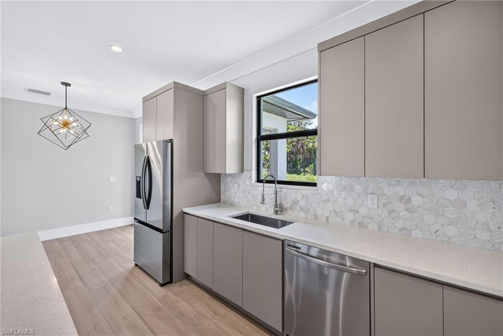 Kitchen featuring light wood-finish flooring, light gray cabinetry, stainless steel appliances, and a hexagonal tile backsplash