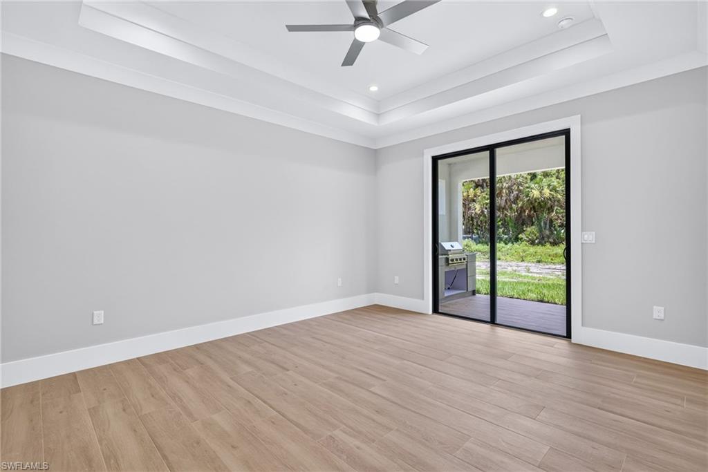 Spacious room featuring wood-finish flooring, light gray walls, and a tray ceiling with recessed lighting and a ceiling fan