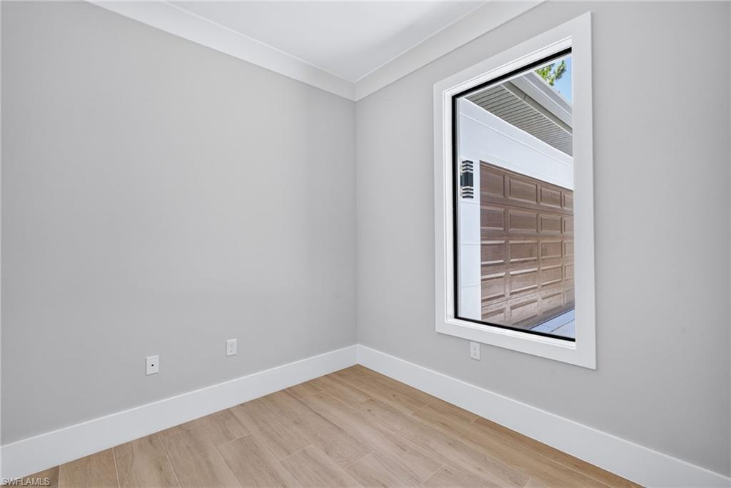 Bright corner bedroom showcasing crisp white walls, polished wood-finish flooring, and abundant natural light from a large window frame