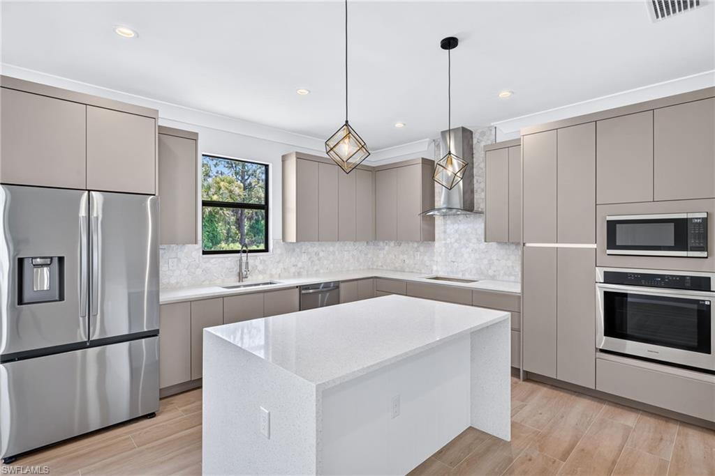 Modern kitchen featuring a central island with a white countertop, stainless steel appliances, light-toned flat-panel cabinetry, a patterned tile backsplash, and wood-finish flooring